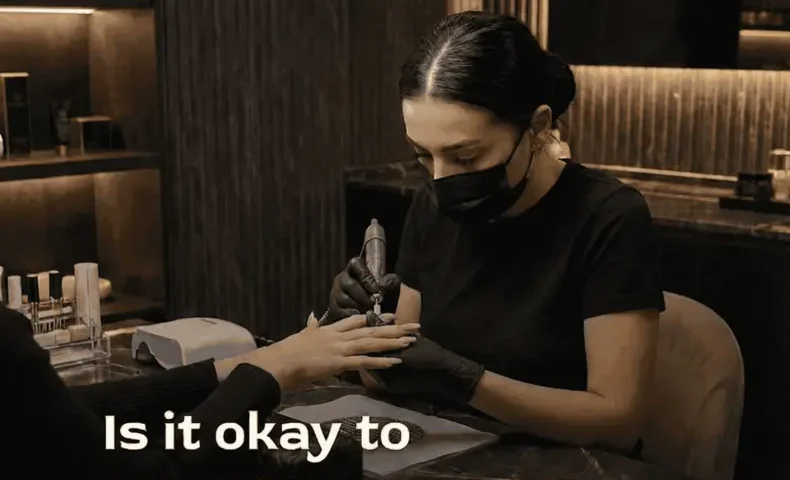 Nail technician shaping a client's nails, wearing a mask and gloves.